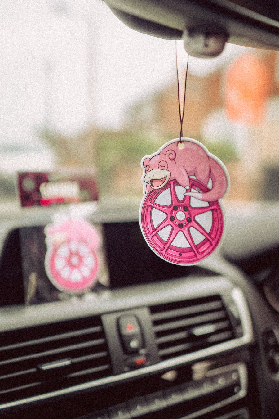 Pink car air freshener with a slowpoke design hanging from a car's rearview mirror.