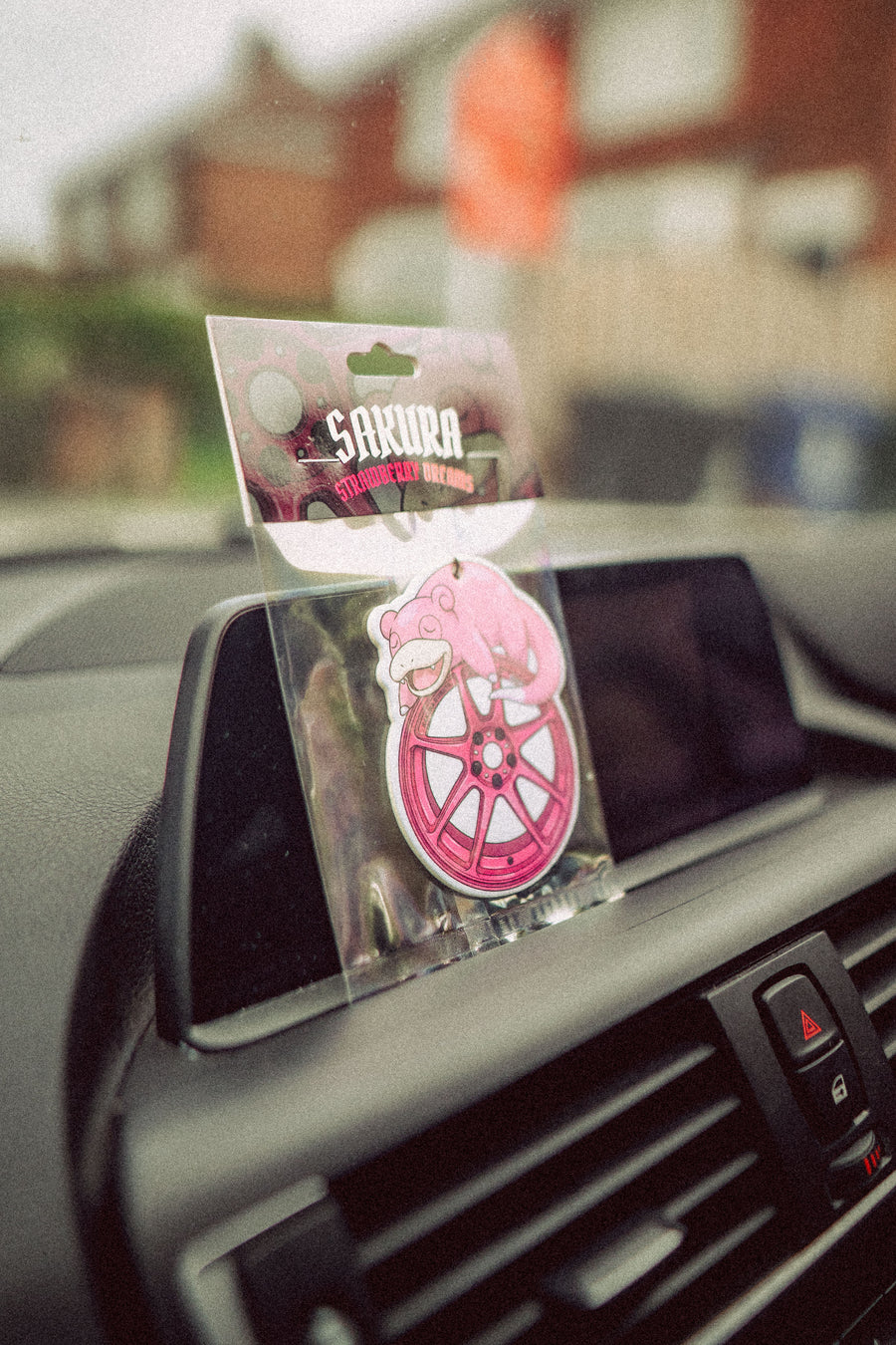 Pink car air freshener in a clear packaging on a car dashboard with a blurred background