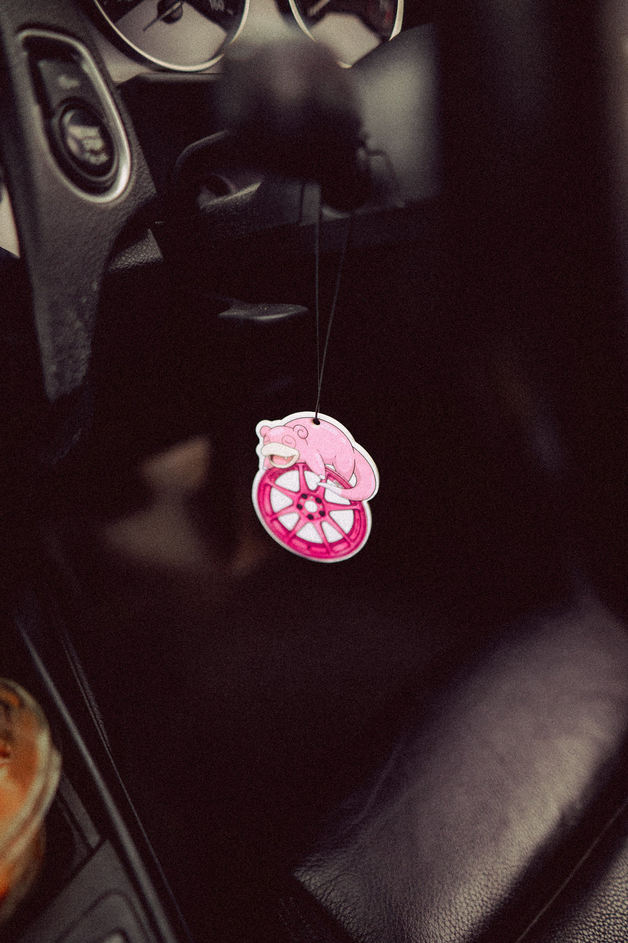Pink car air freshener with a cartoon character hanging from a car's dashboard.