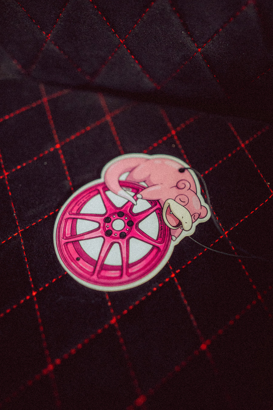 Pink car wheel rim with slowpoke design on a dark quilted background