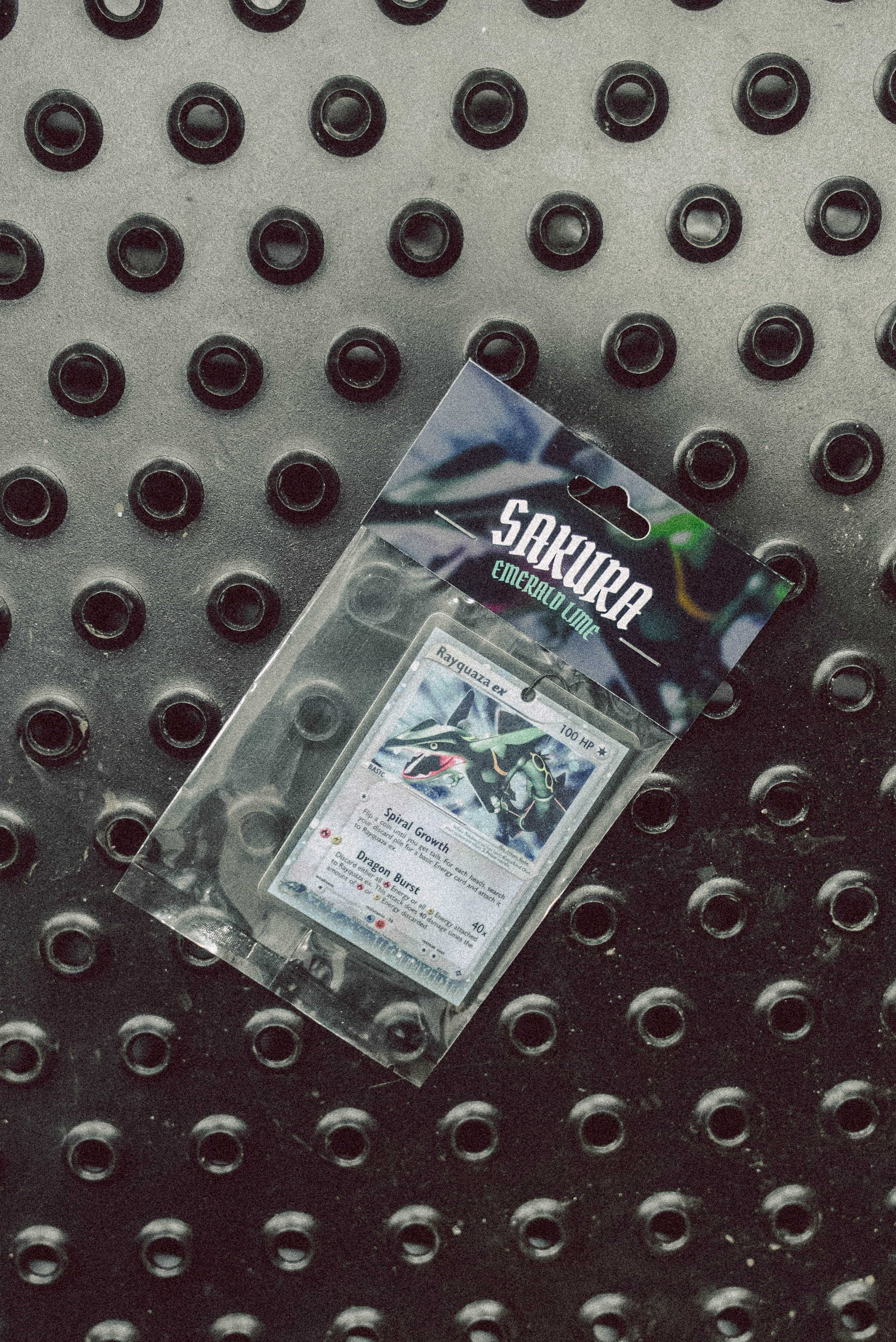 Sakura Trading Card Game card on a concrete surface with a car tire in the background