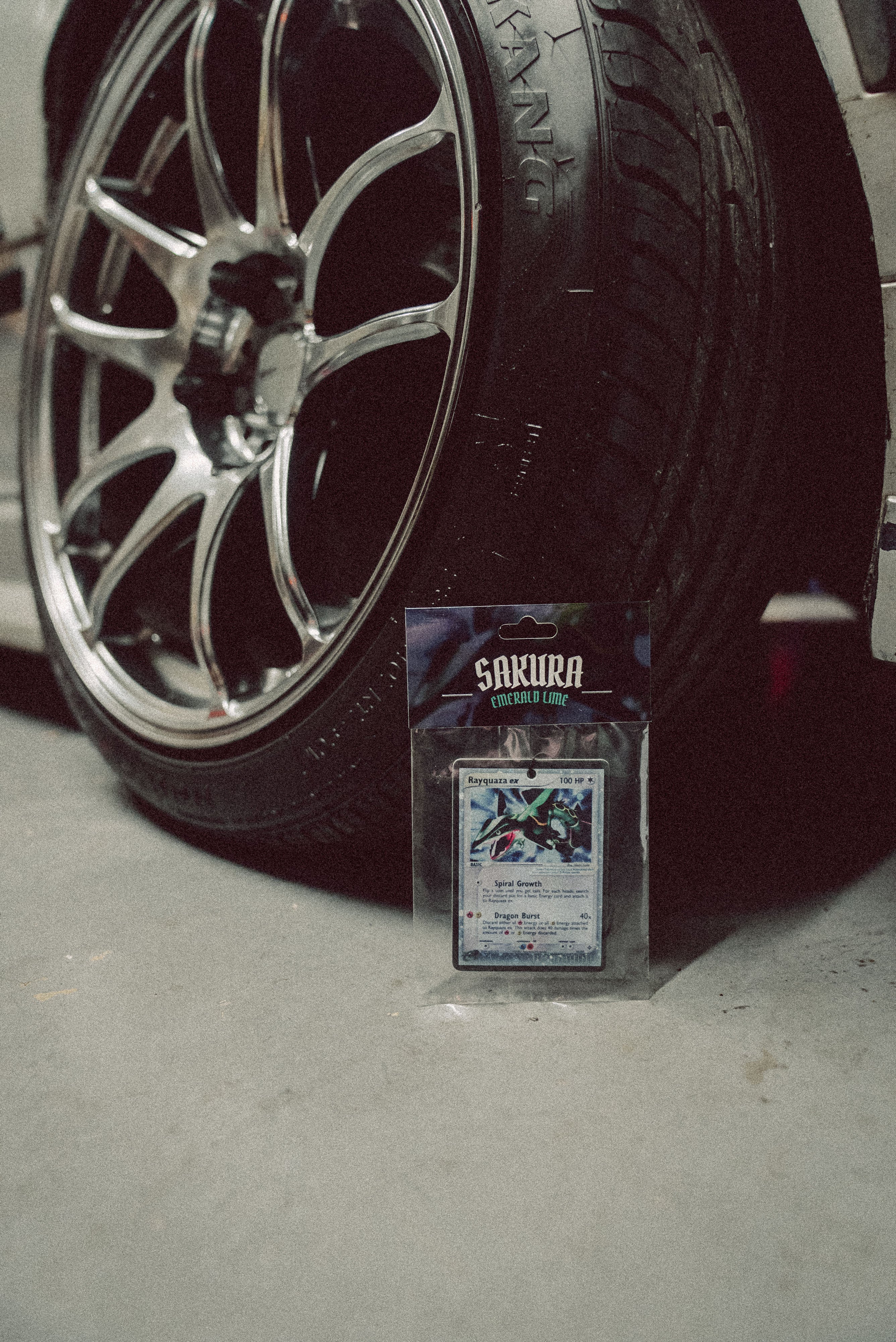Sakura Trading Card Game card on a concrete surface with a car tire in the background