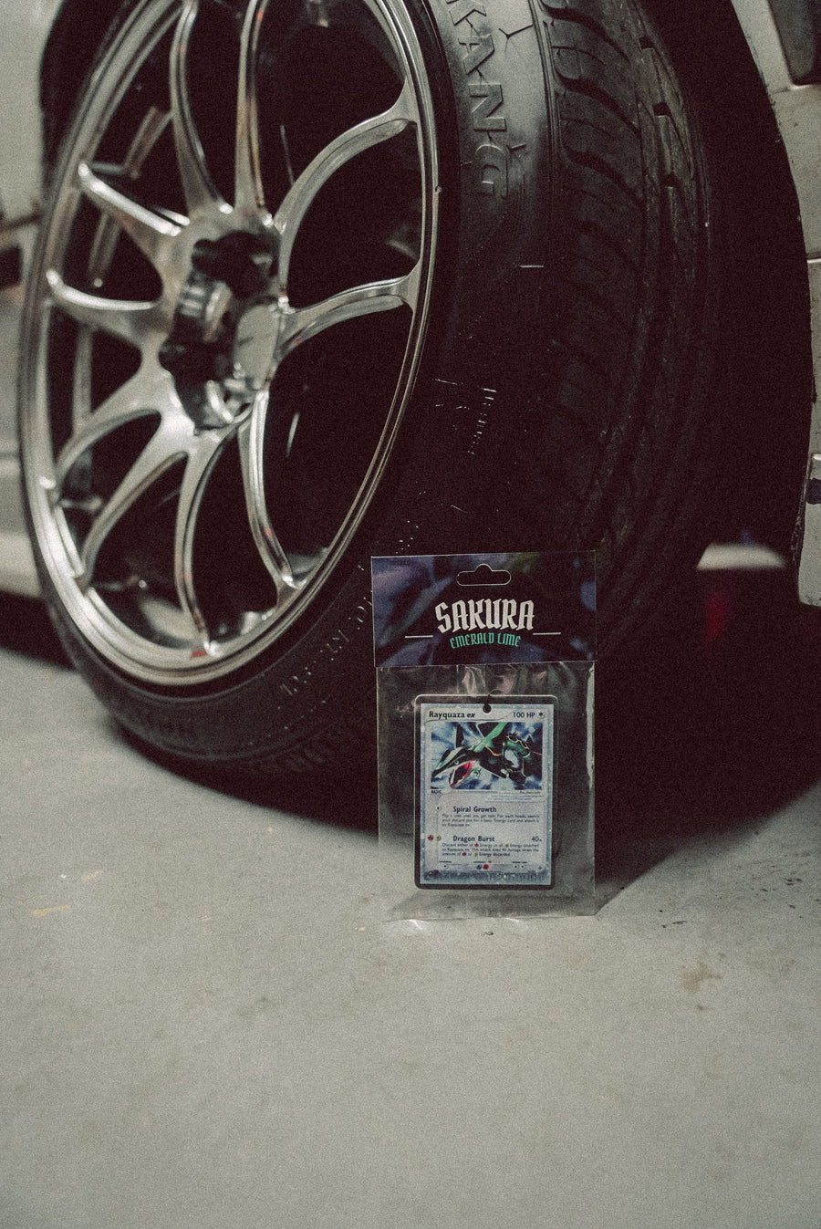 Sakura Trading Card Game card on a concrete surface with a car tire in the background