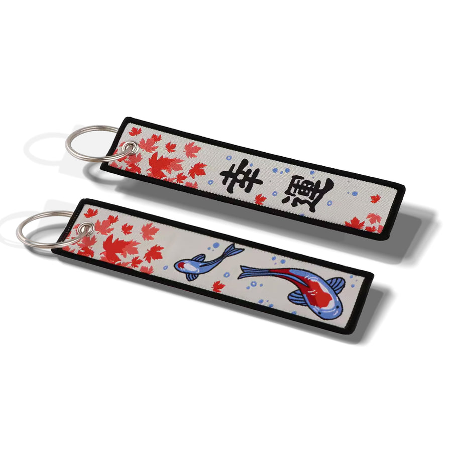 Two rectangular keychains with silver split rings, featuring a white background decorated with red floral patterns, black kanji characters, and blue and red koi fish, shown on a white background.