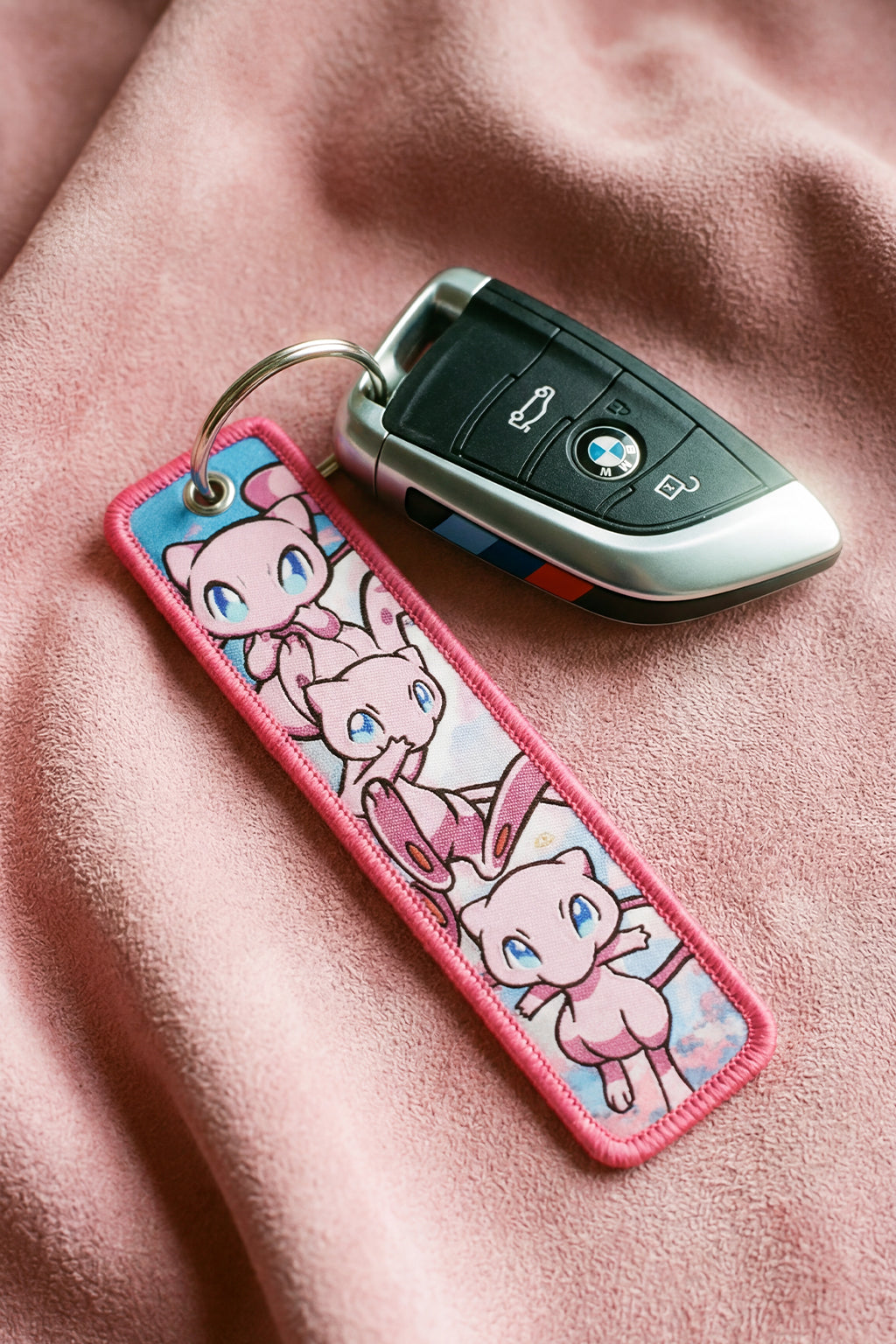 Keychain with cartoon mew design attached to a car key on a pink fabric background