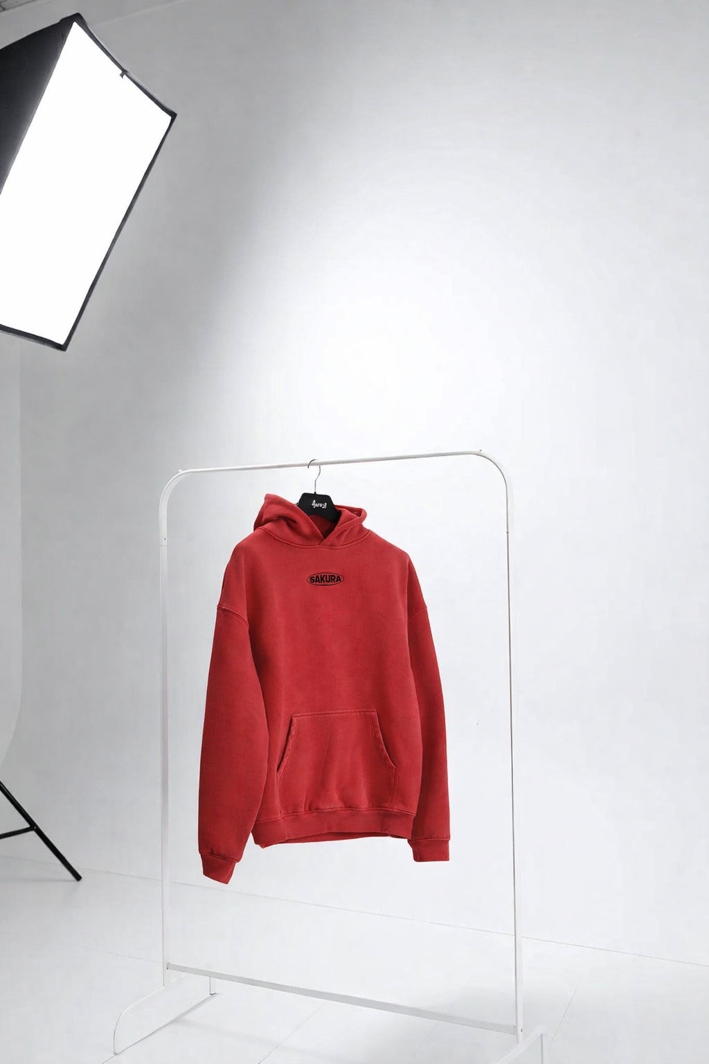 Red hoodie on a hanger against a white background with studio lighting equipment.