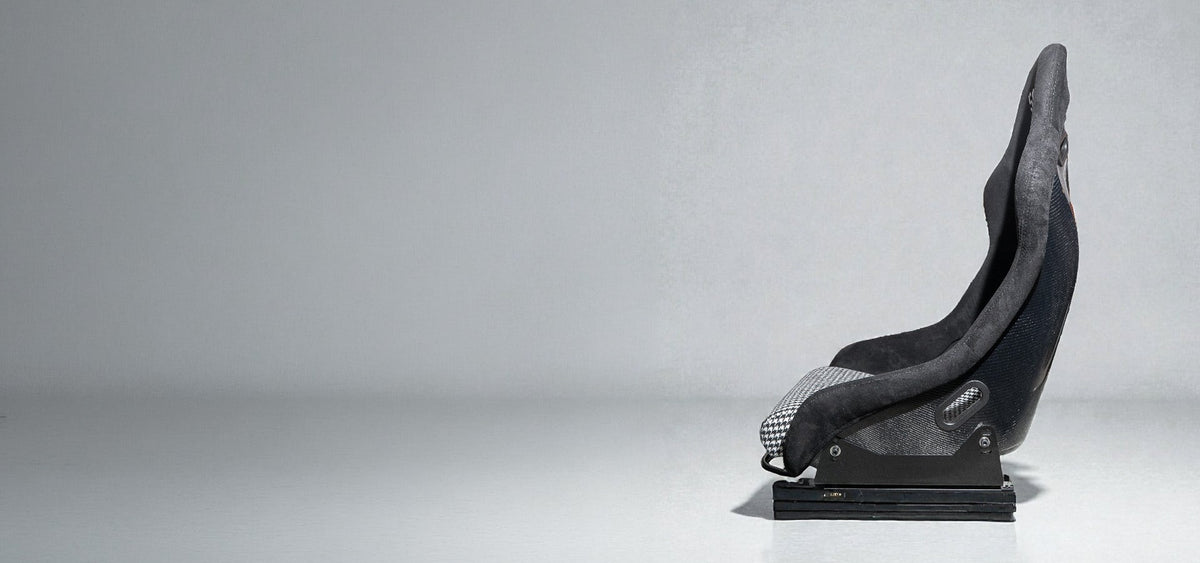 carbon bucket seat on a slightly reflective surface with a white background