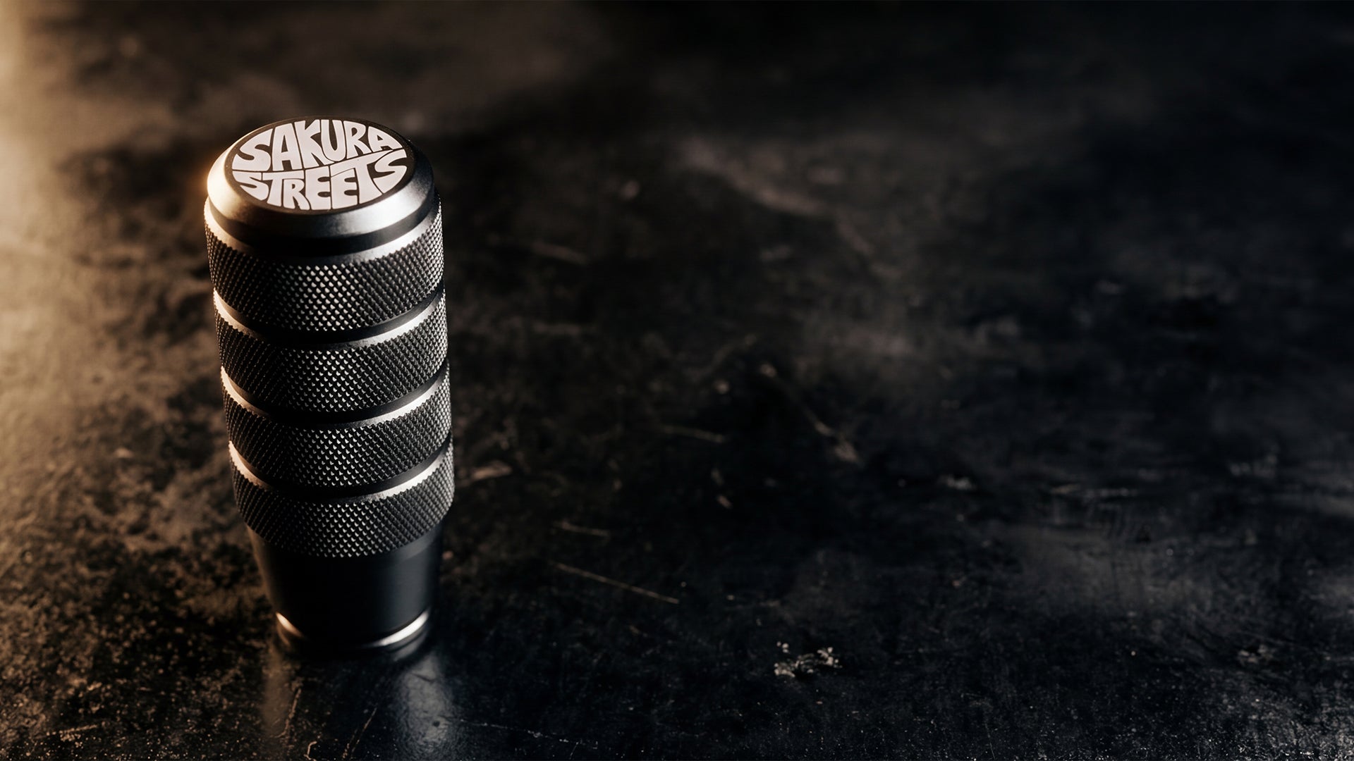 Metal knob with 'Sakura Streets' branding on a dark textured surface