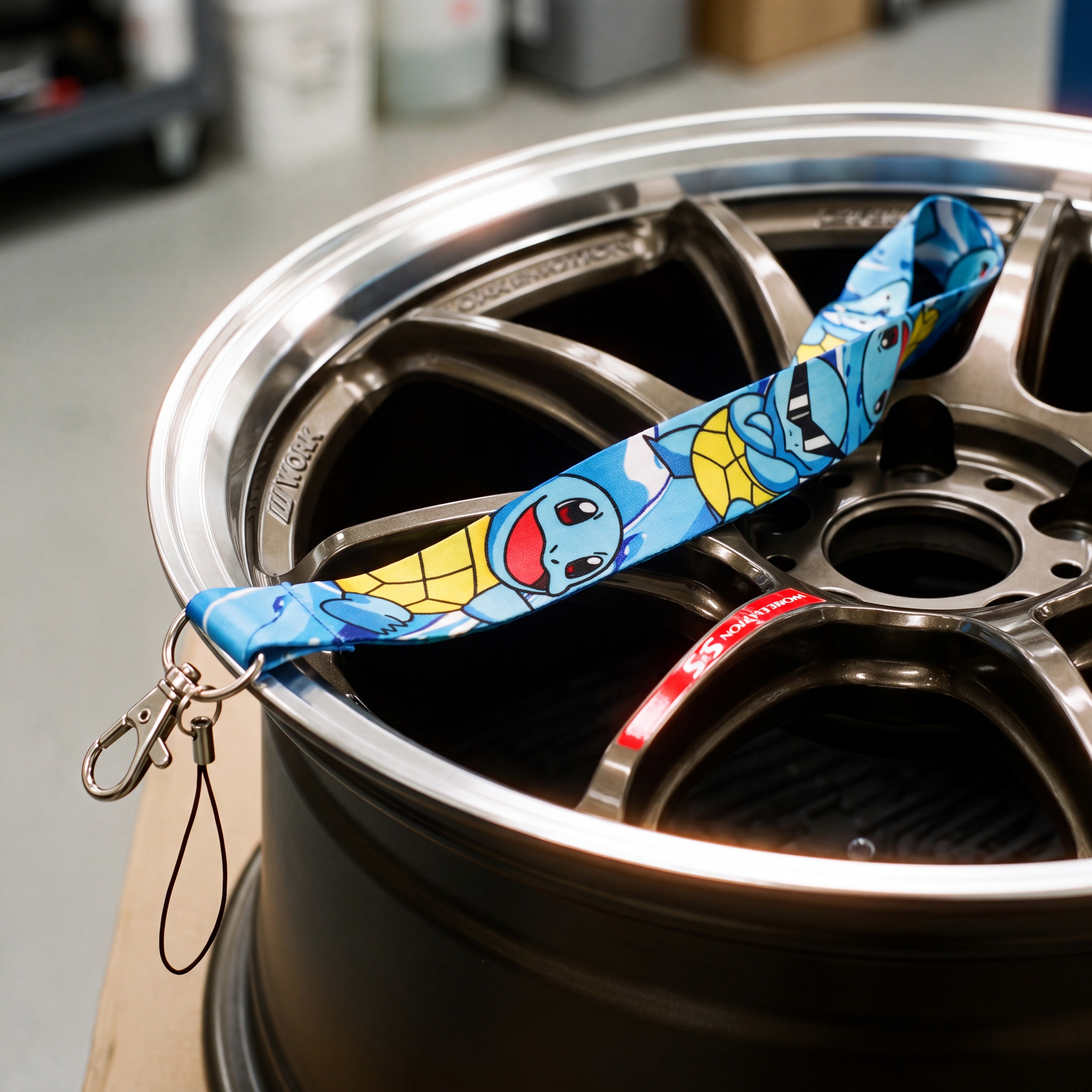 A close-up of a blue and yellow Squirtle lanyard draped over a dark metallic car wheel rim.