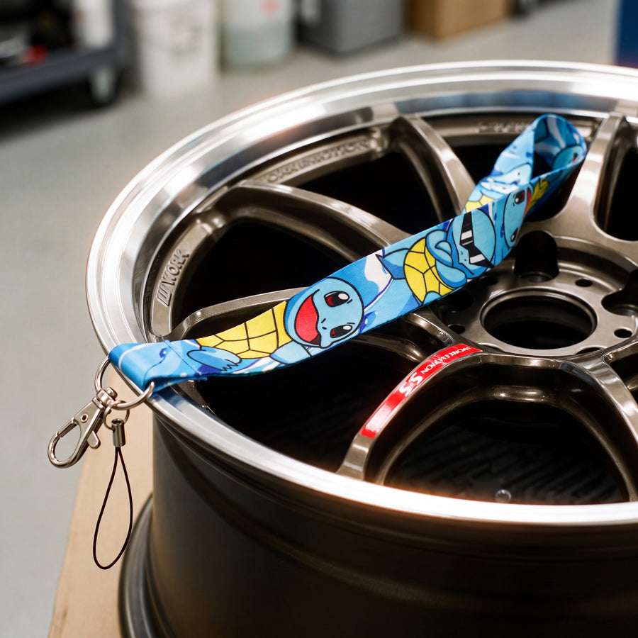A close-up of a blue and yellow Squirtle lanyard draped over a dark metallic car wheel rim.