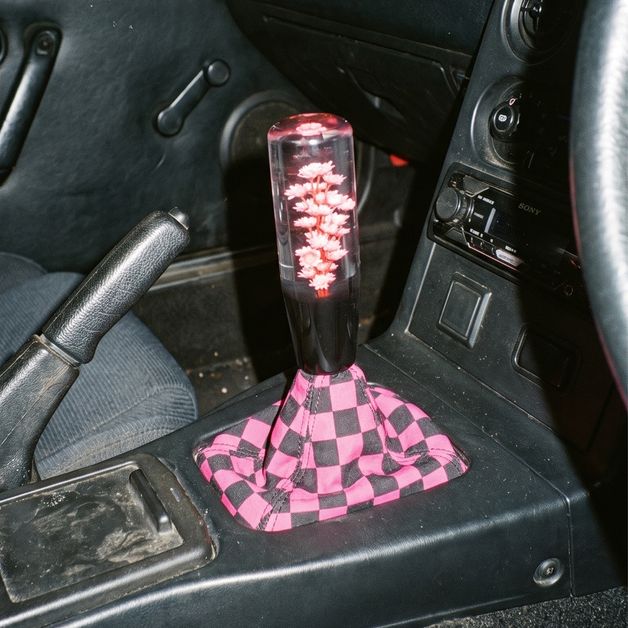 Car interior with a pink and black checkered gear shift cover.