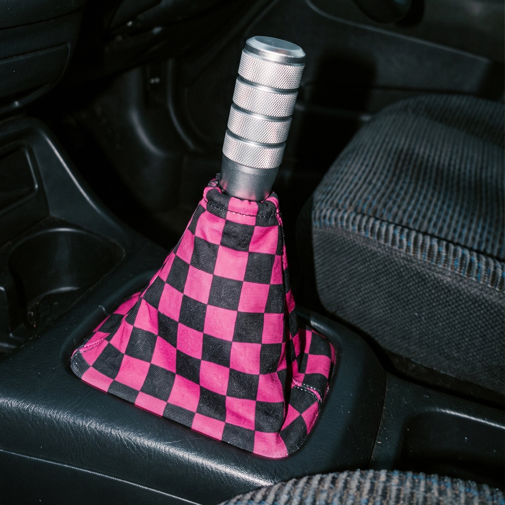 Car gear shift with a pink and black checkered cover inside a vehicle.